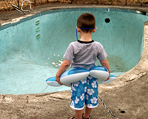 boy with rubber ring stands by empty disused swimming pool